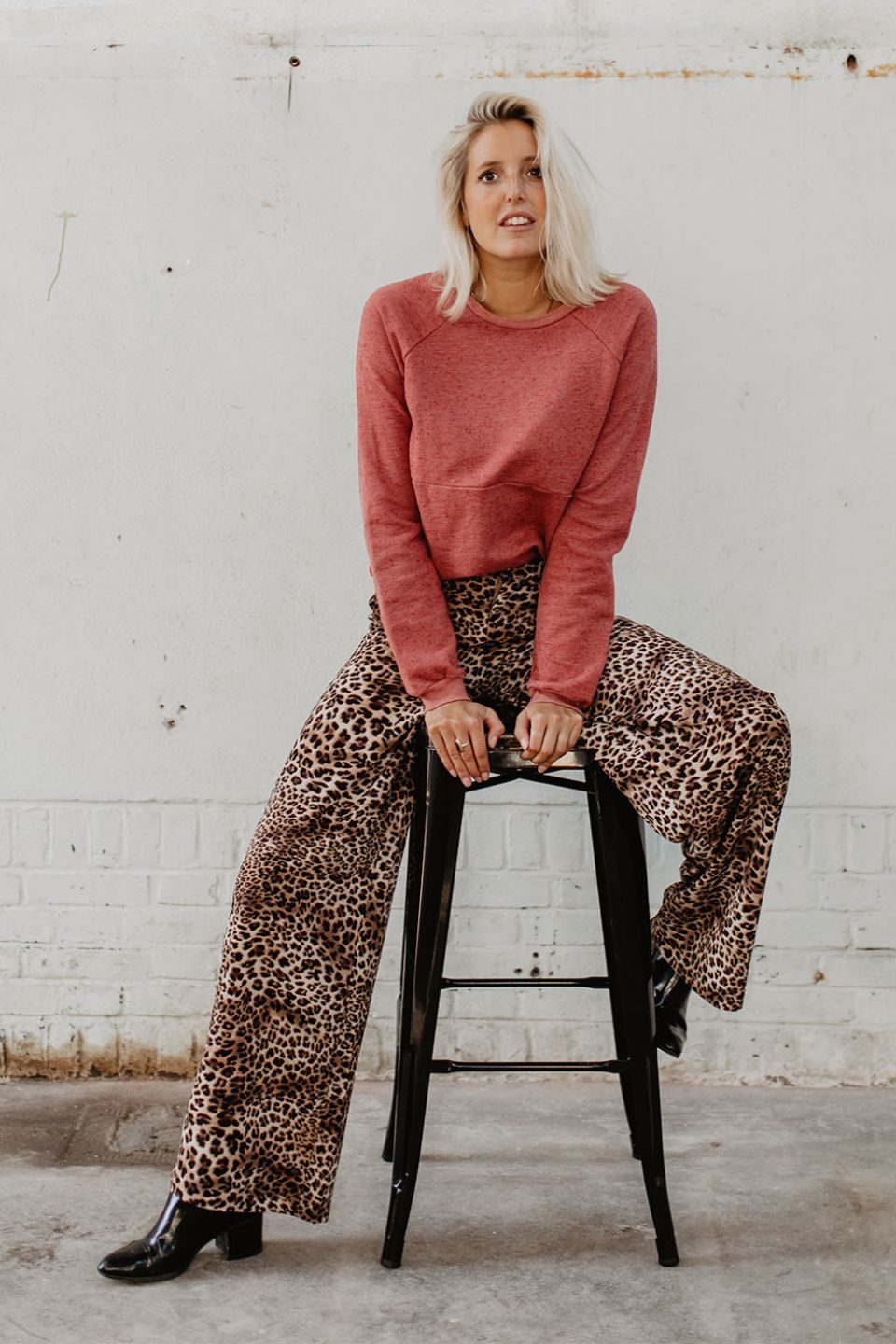 Meisje in industrieel pand met een Loavies luipaardprint broek en een zalmroze modstrom trui.